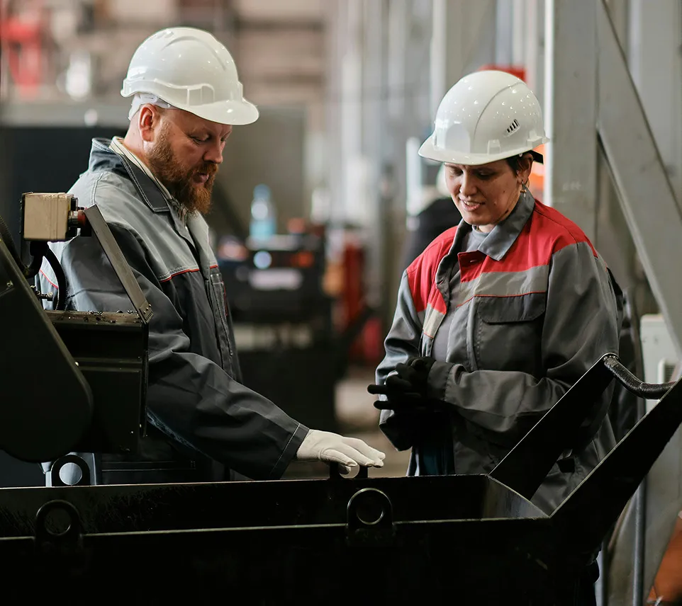 Two workers standing next to black bin in factory